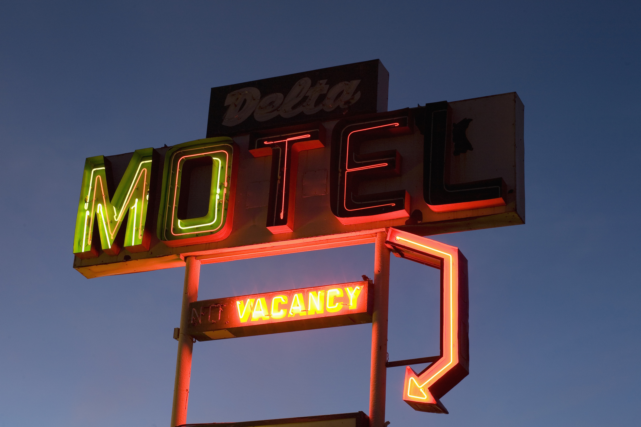 Neon sign for Delta Motel at dusk, with a lit &quot;NO VACANCY&quot; notice