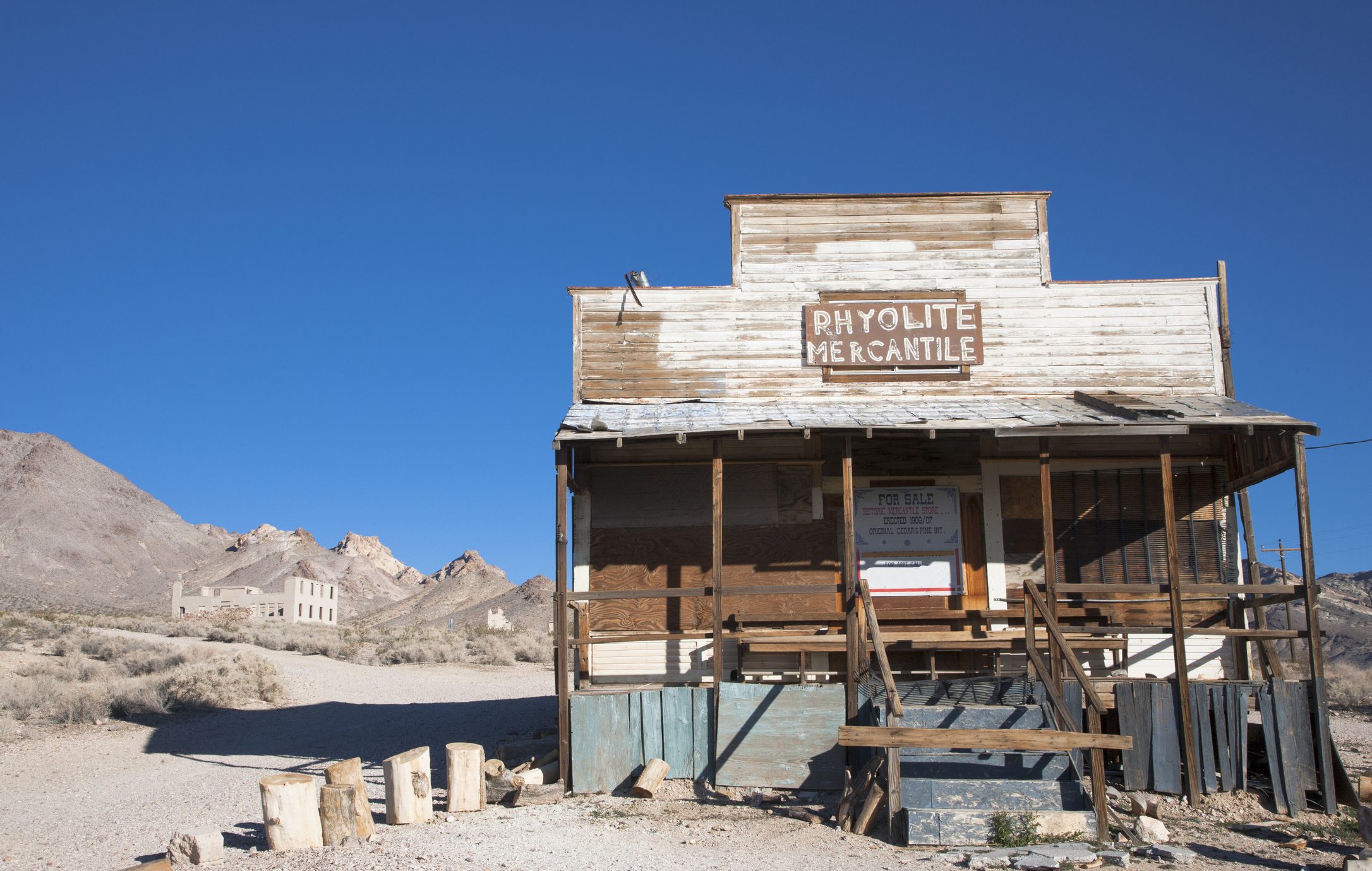 Old wooden building labeled &quot;Rhyolite Mercantile&quot; with abandoned structures in a desert background