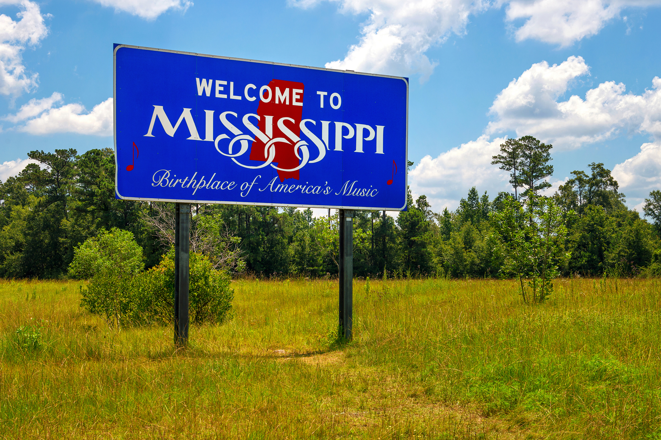 Welcome sign reading &quot;Welcome to Mississippi, Birthplace of America&#x27;s Music&quot; with trees and sky in the background