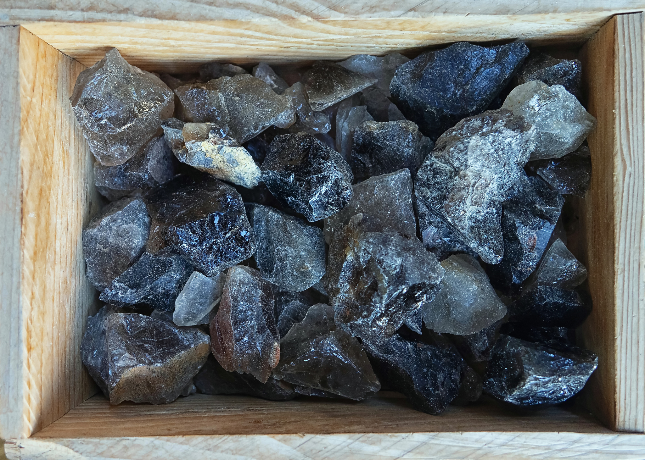 A wooden tray filled with various pieces of raw smoky quartz crystals