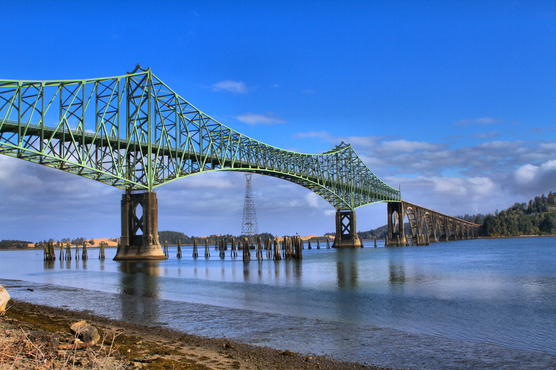A truss bridge spans a river under a partly cloudy sky