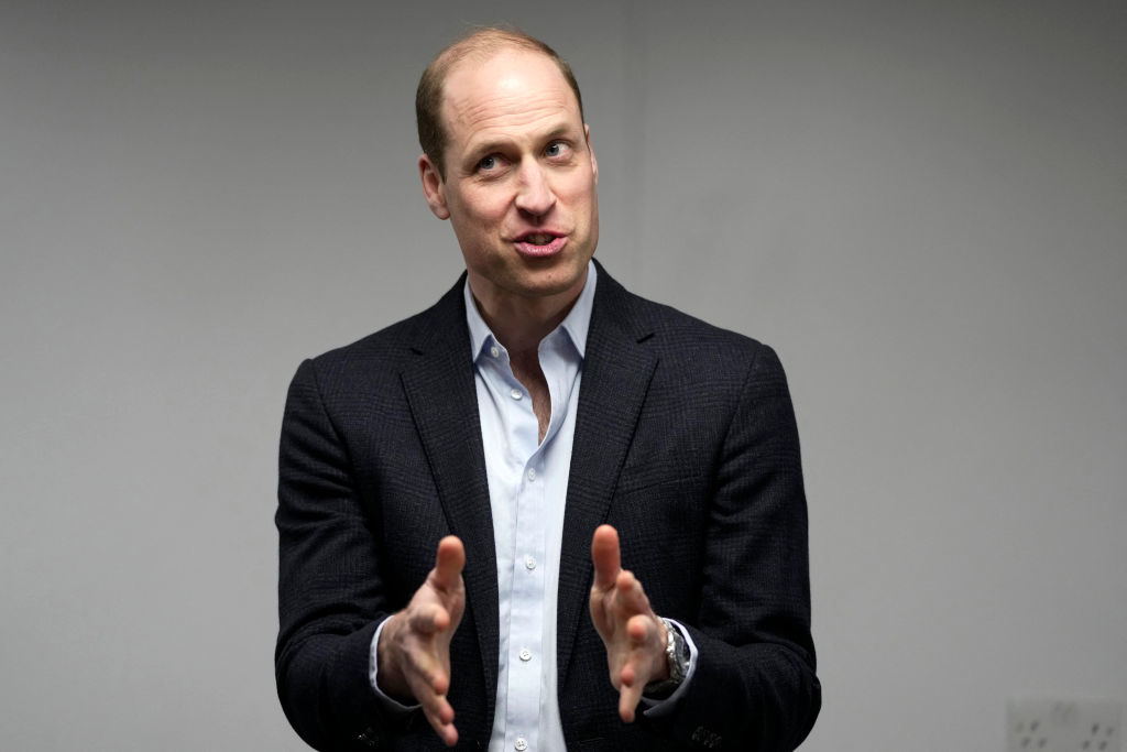 William in a dark blazer and light shirt gesturing while speaking indoors