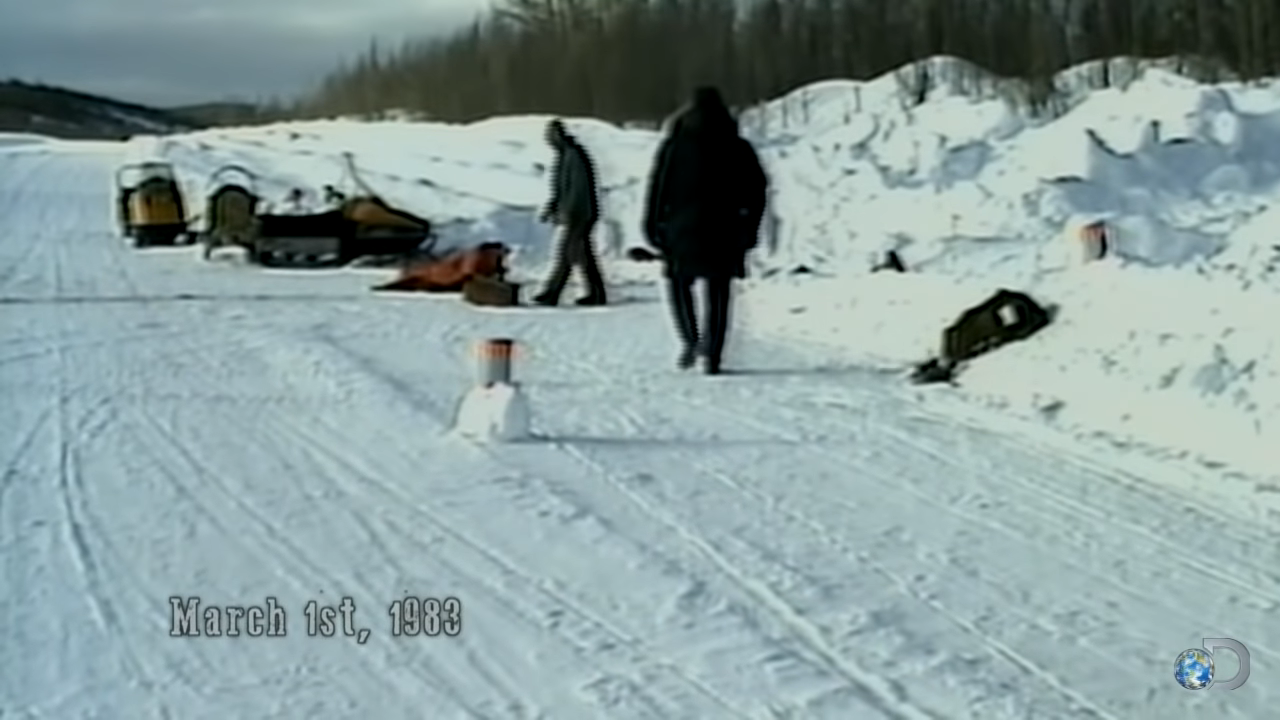 Two people and a dog are on a snowy road with equipment, dated March 1st, 1983