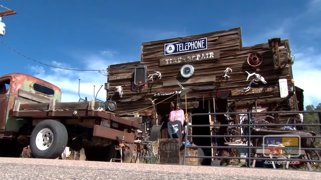 Old truck parked in front of a rustic building with eclectic decor and signs stating &quot;Telephone&quot; and &quot;Tire Repair.&quot;