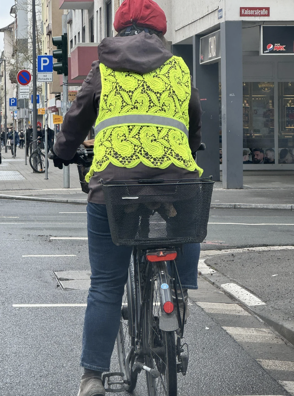 Person on a bicycle wearing a high-visibility vest, viewed from behind