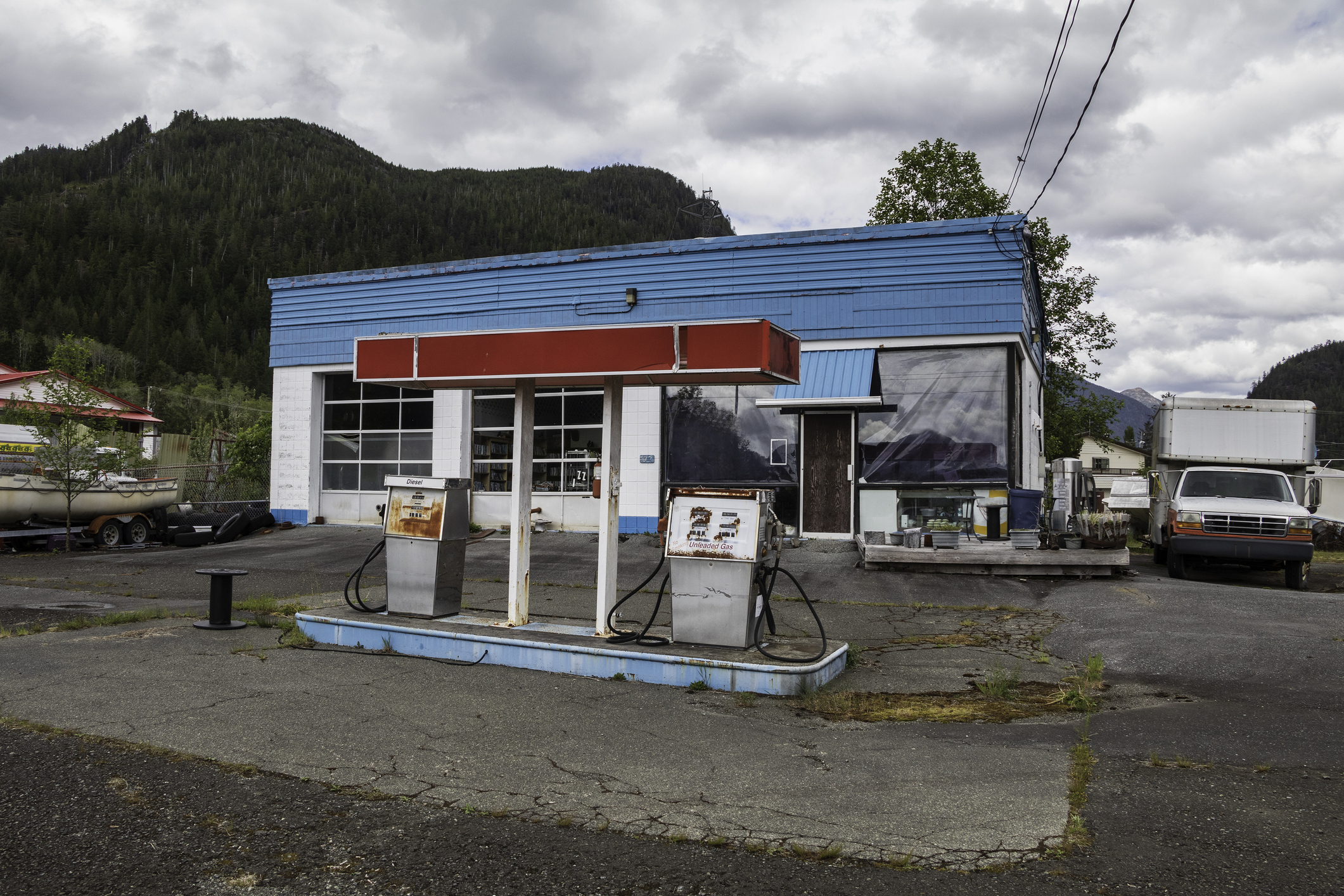 Old gas station with two pumps and a blue building against a mountainous backdrop