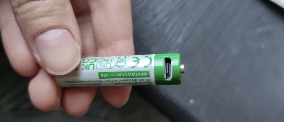 Hand holding a green AA battery with recycling symbols and instructions