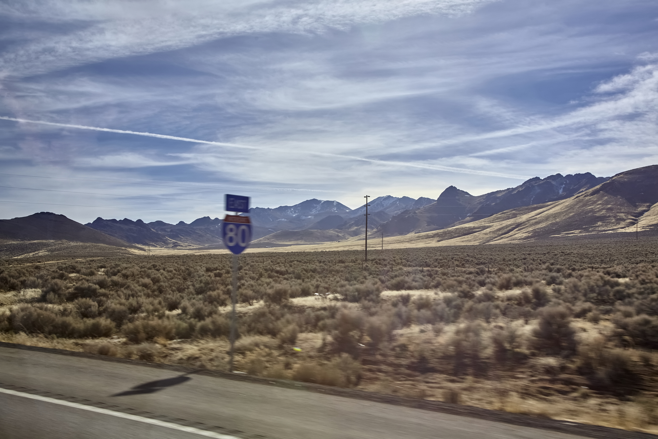 Interstate 80 sign beside a highway with distant mountains and clear skies