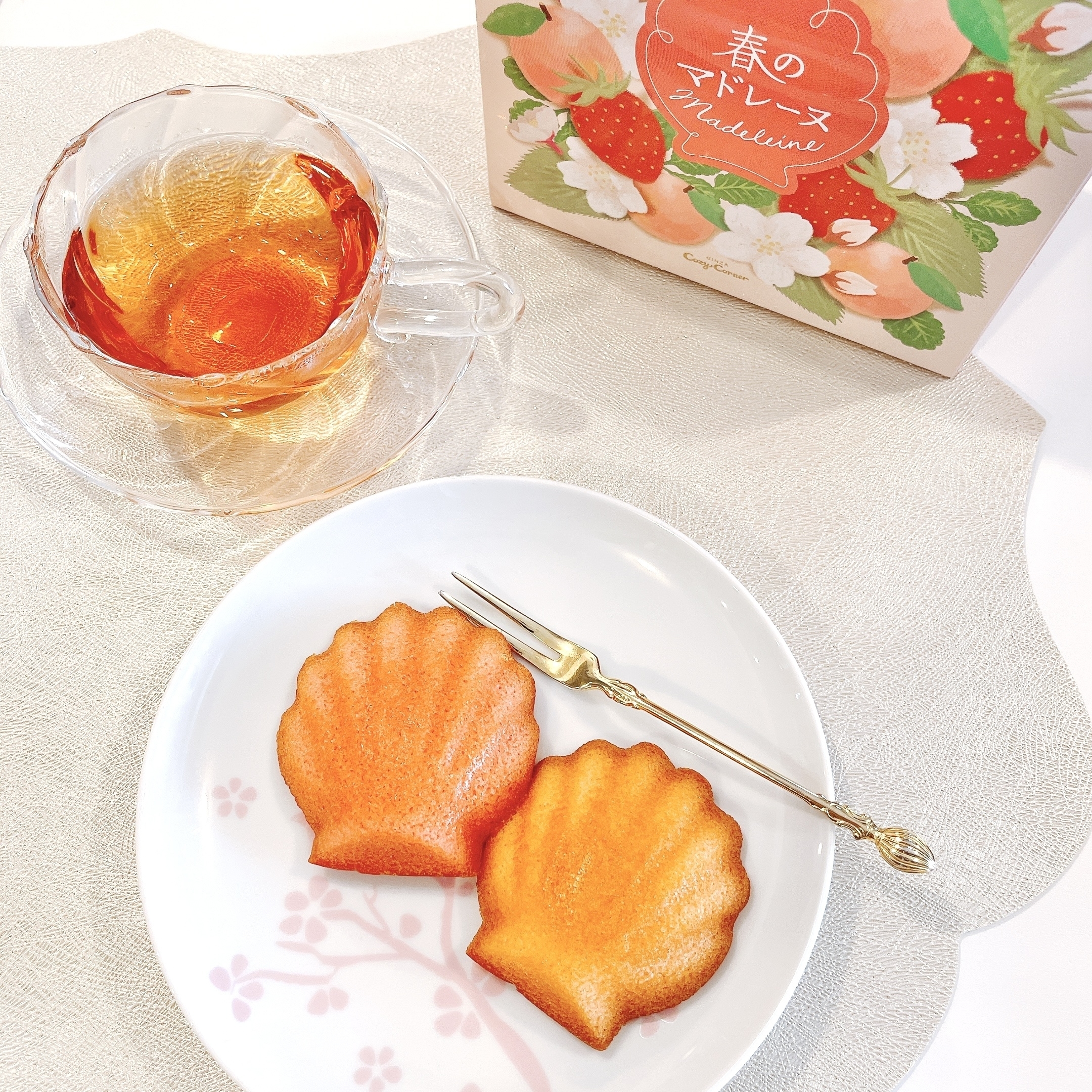 透明なカップに入った飲み物とお皿の上のスポンジケーキ、背景にパッケージ。