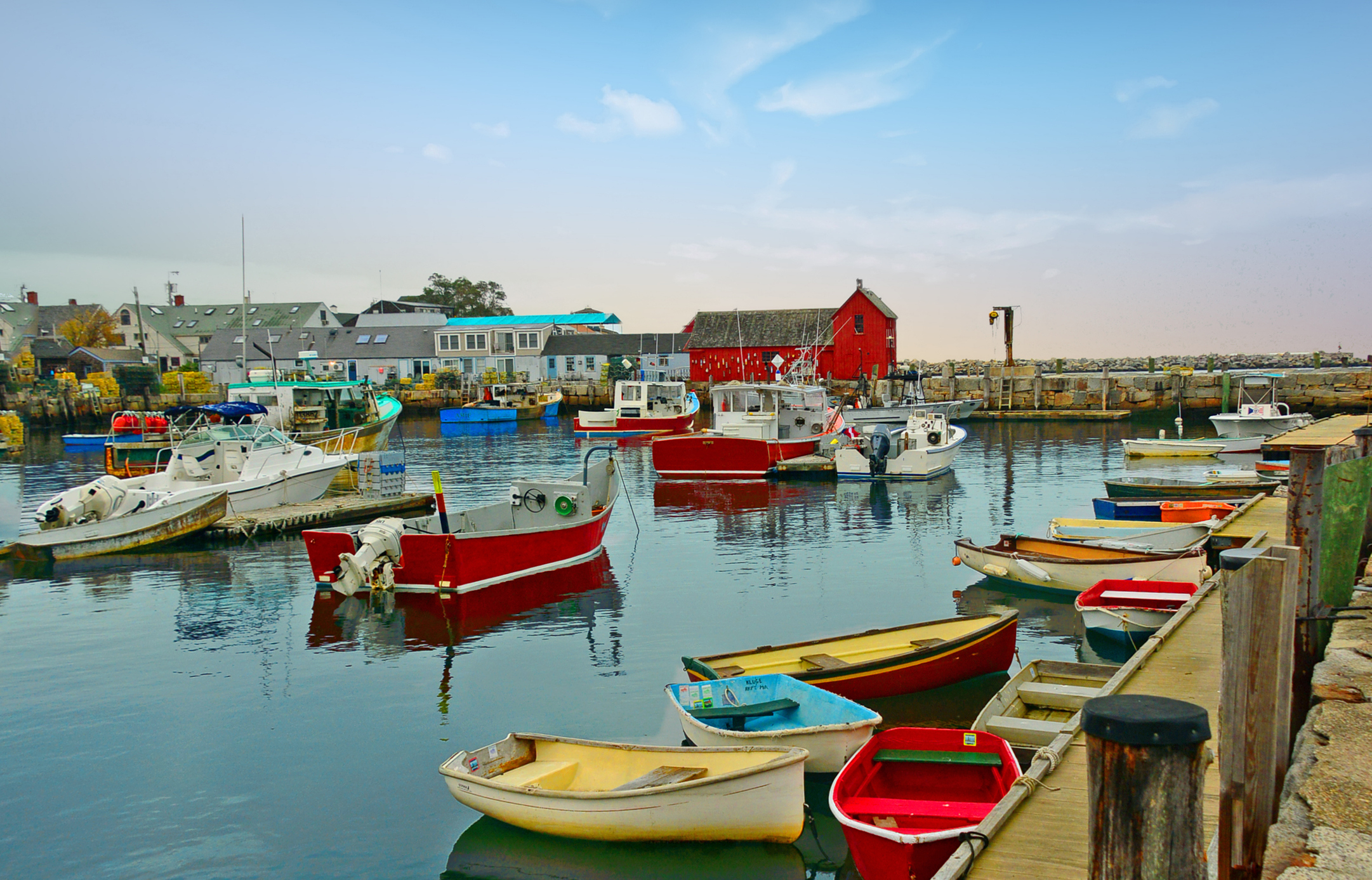 Fishing boats and dinghies docked by a waterfront with buildings and a red shack