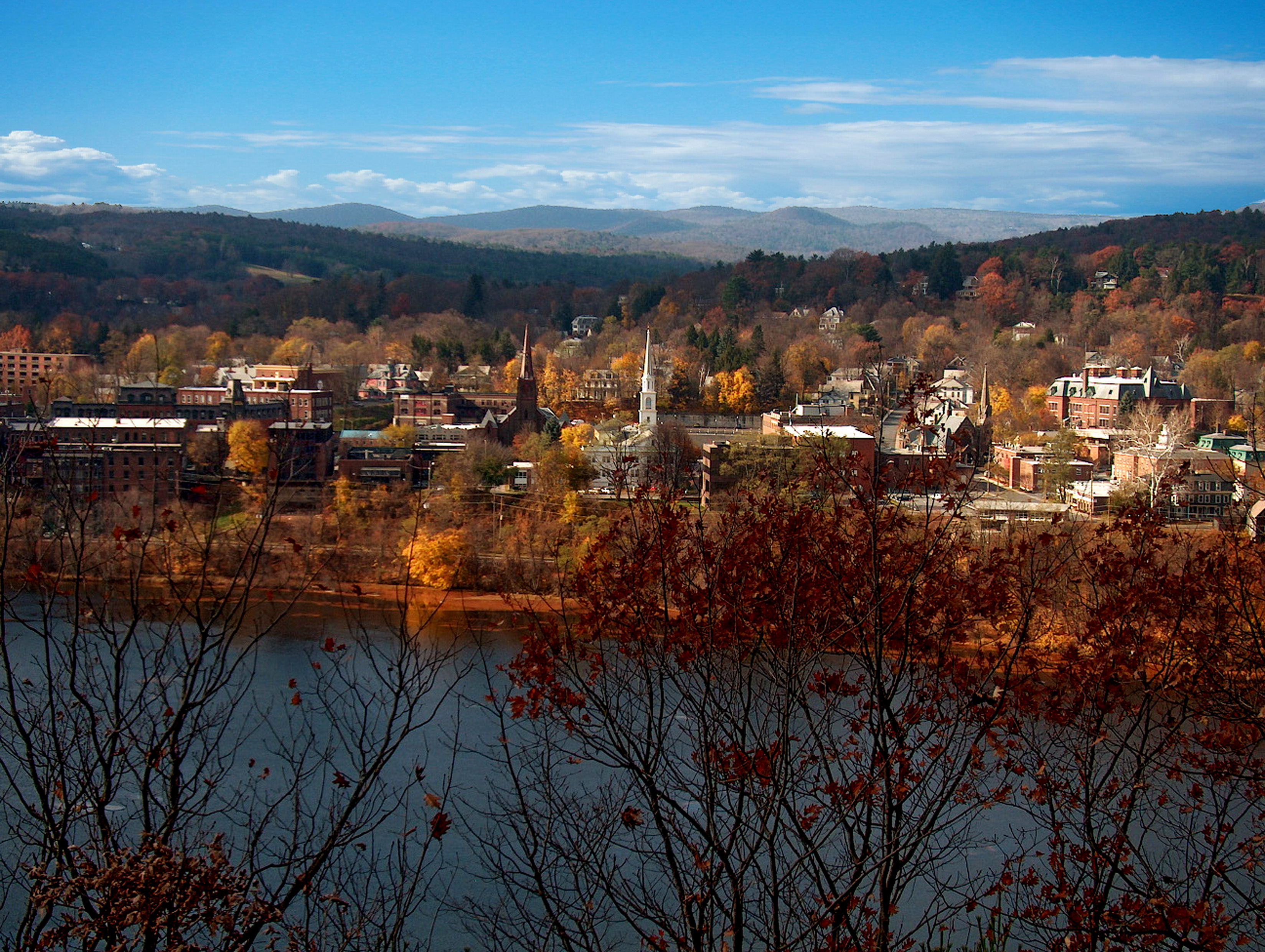 Scenic view of a town with buildings amid autumn trees and distant hills