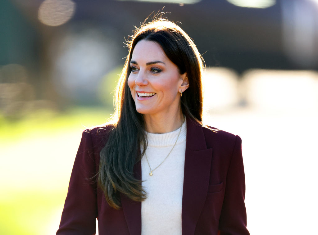Kate Middleton smiles wearing a blazer, outdoors at a public event