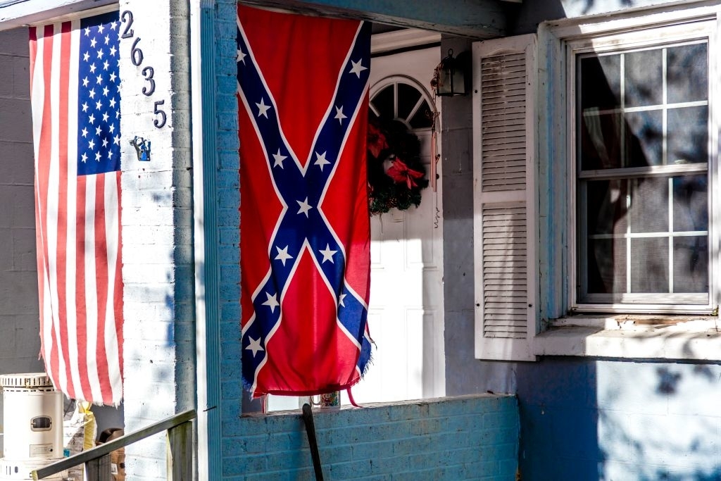 An American flag and a Confederate flag hang side by side on a house&#x27;s front porch