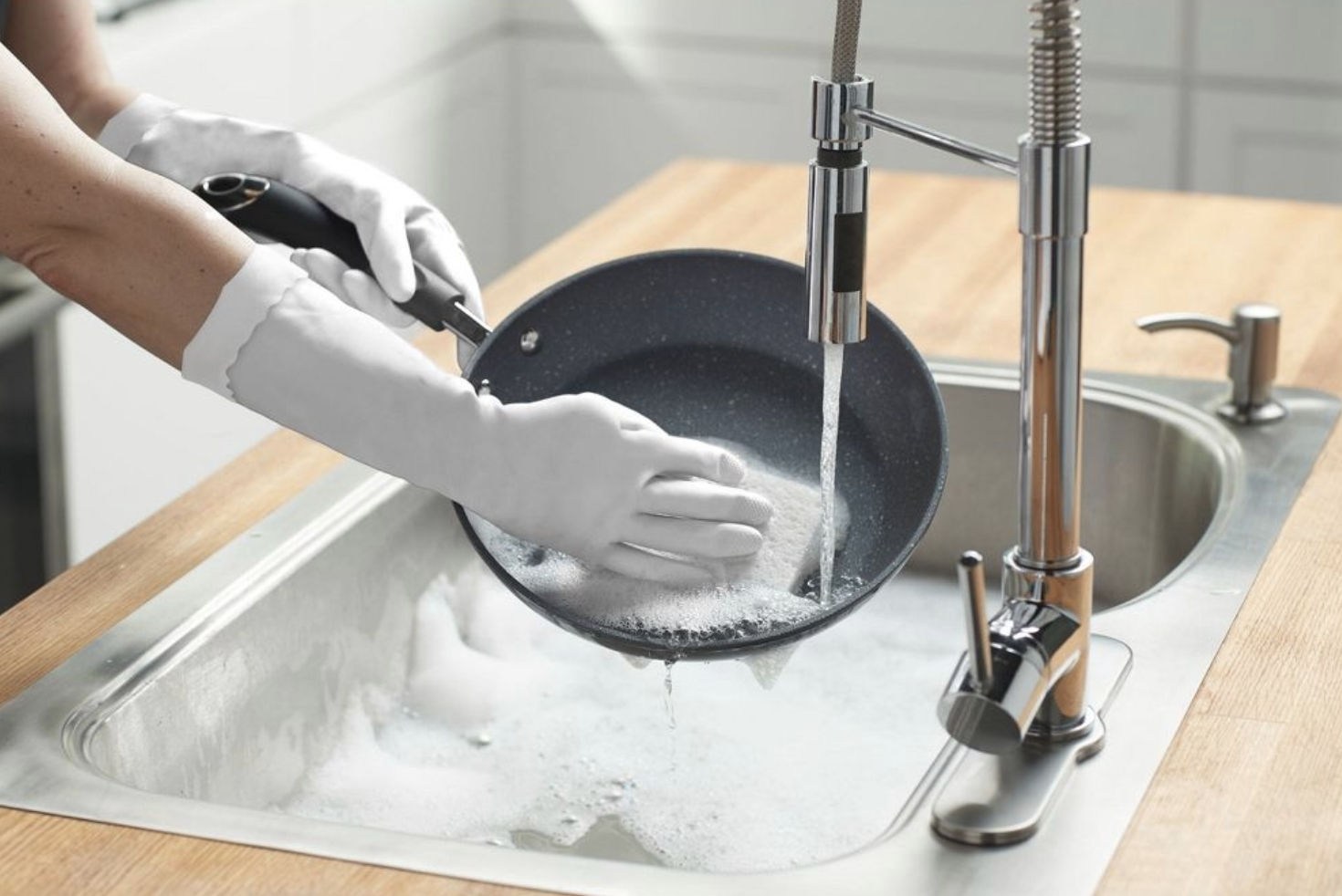 Person washing a non-stick frying pan in a kitchen sink with soapy water