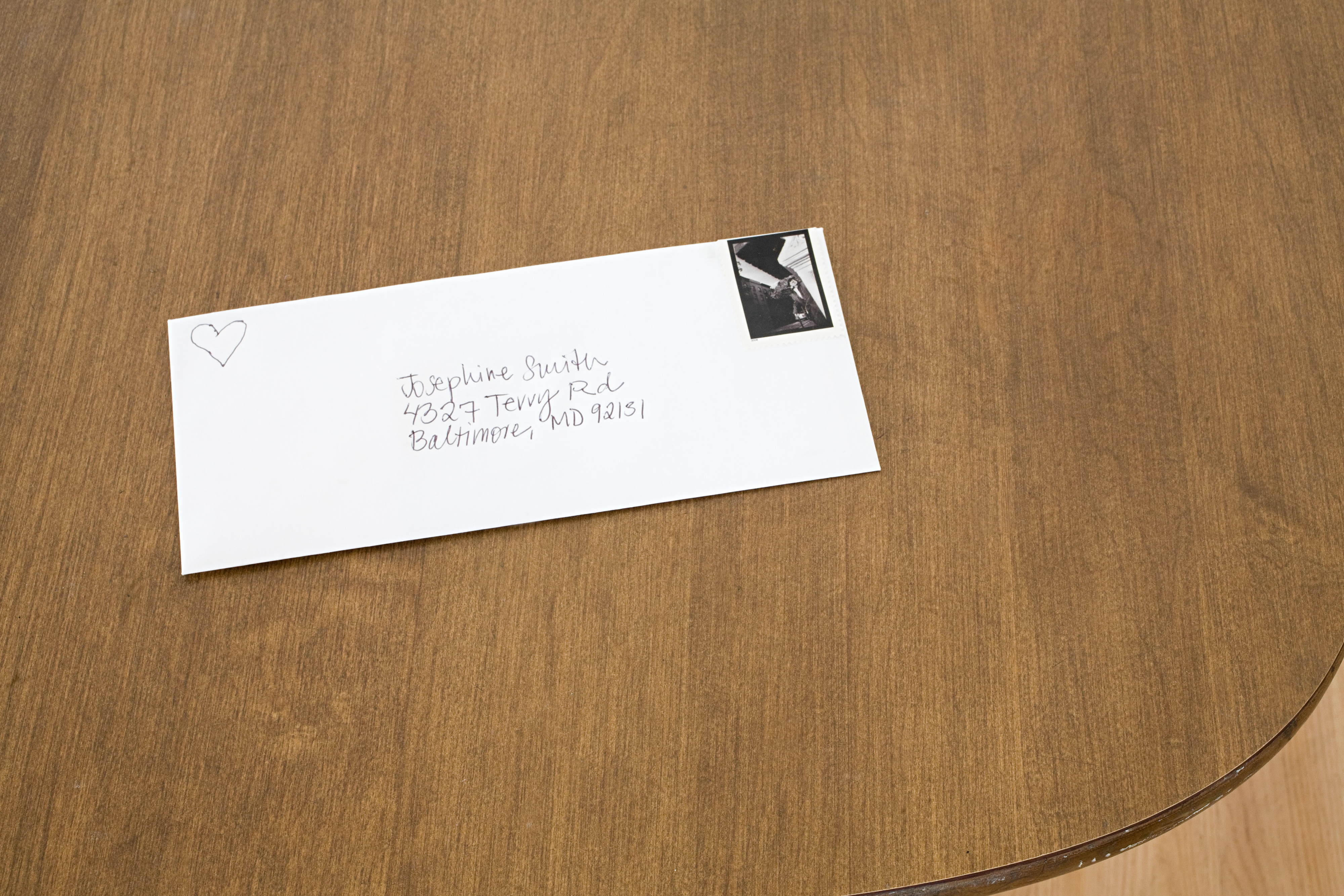 Envelope with hand-written address and heart doodle on wooden surface