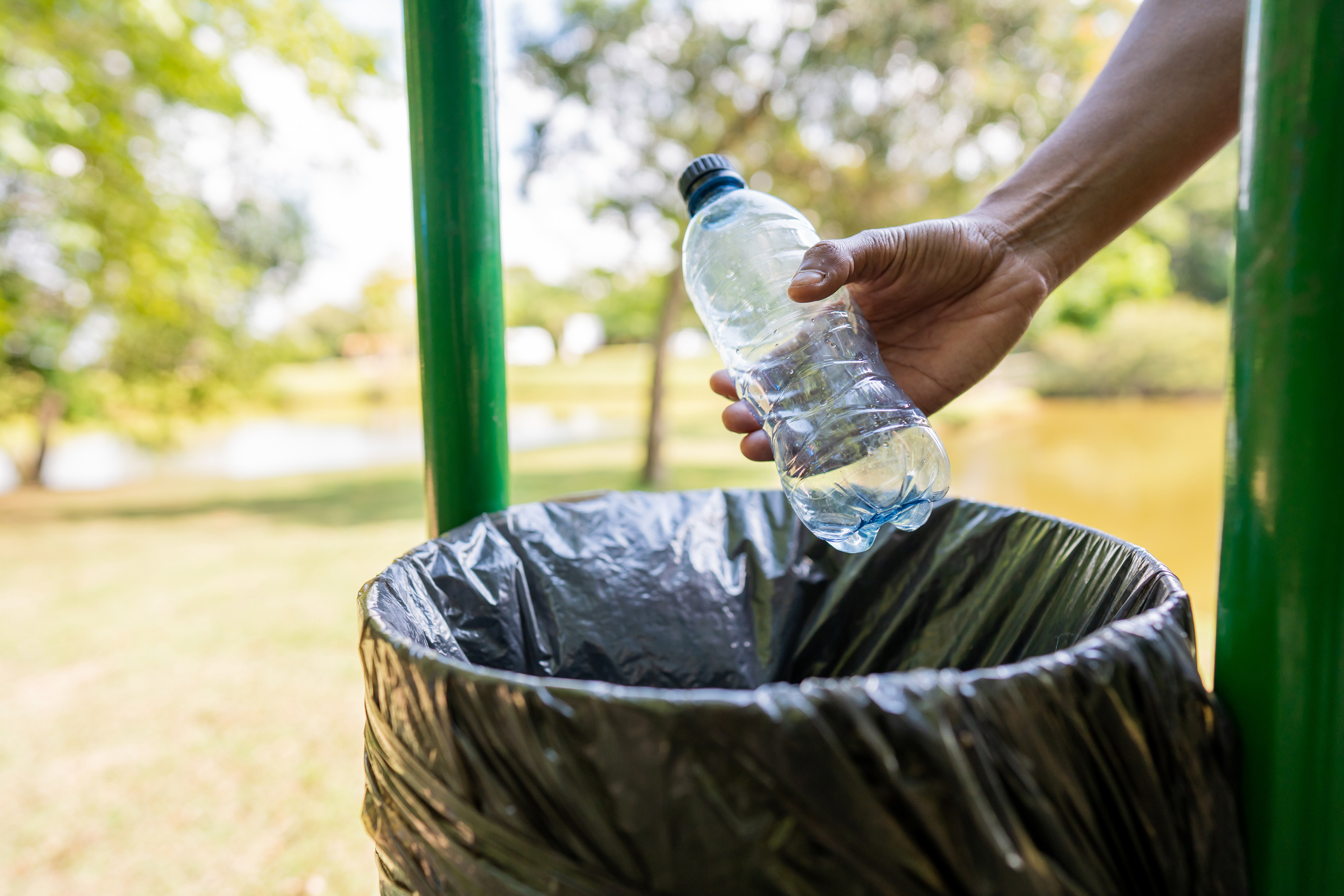 Person disposing of a plastic bottle in a trash bin outdoors