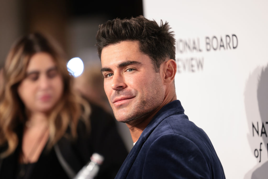 Person in a dark jacket at an event, looking to the side, with blurred background