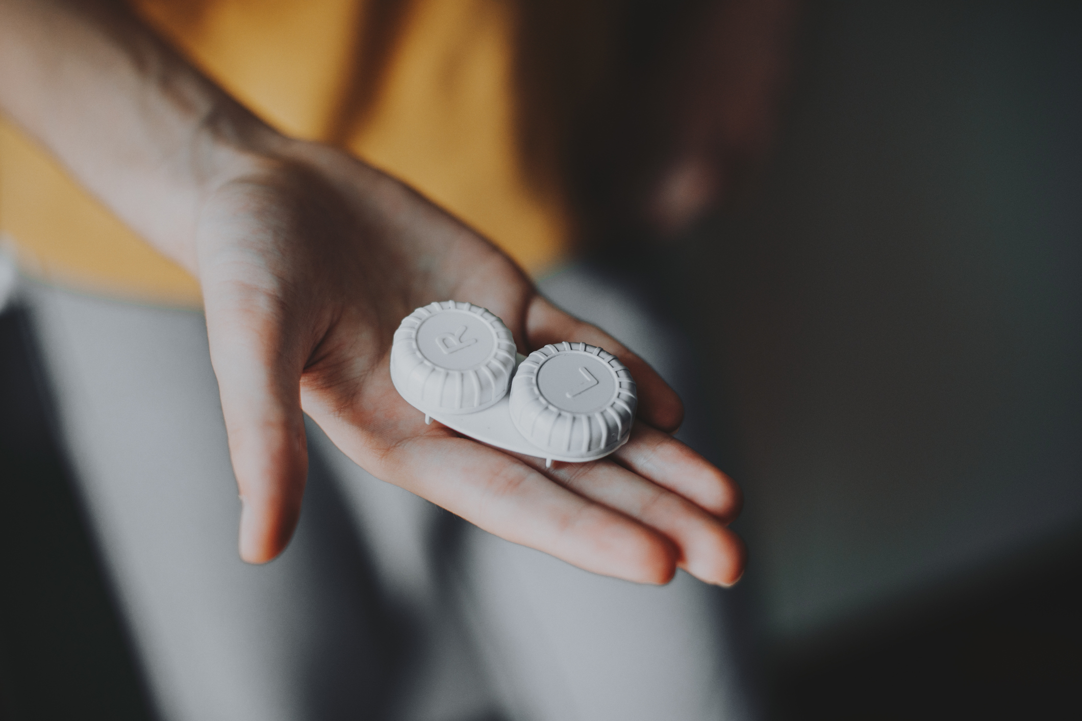 Close-up of a hand holding two contact lens cases marked L and R