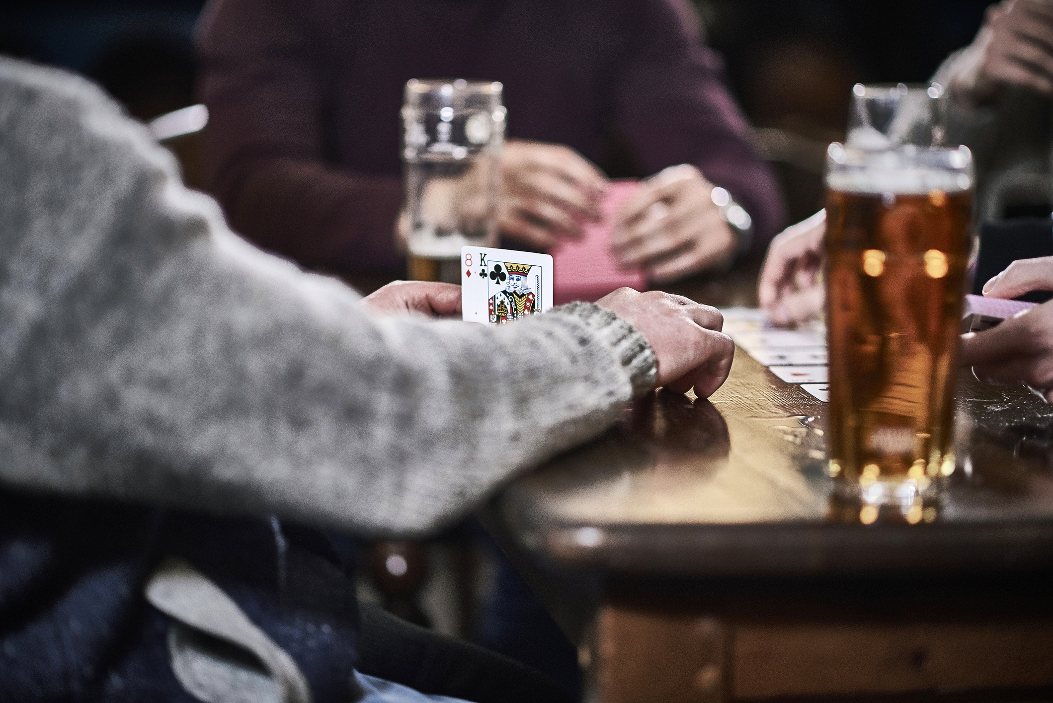 People playing cards with a hand revealing a king of hearts, at a table with drinks