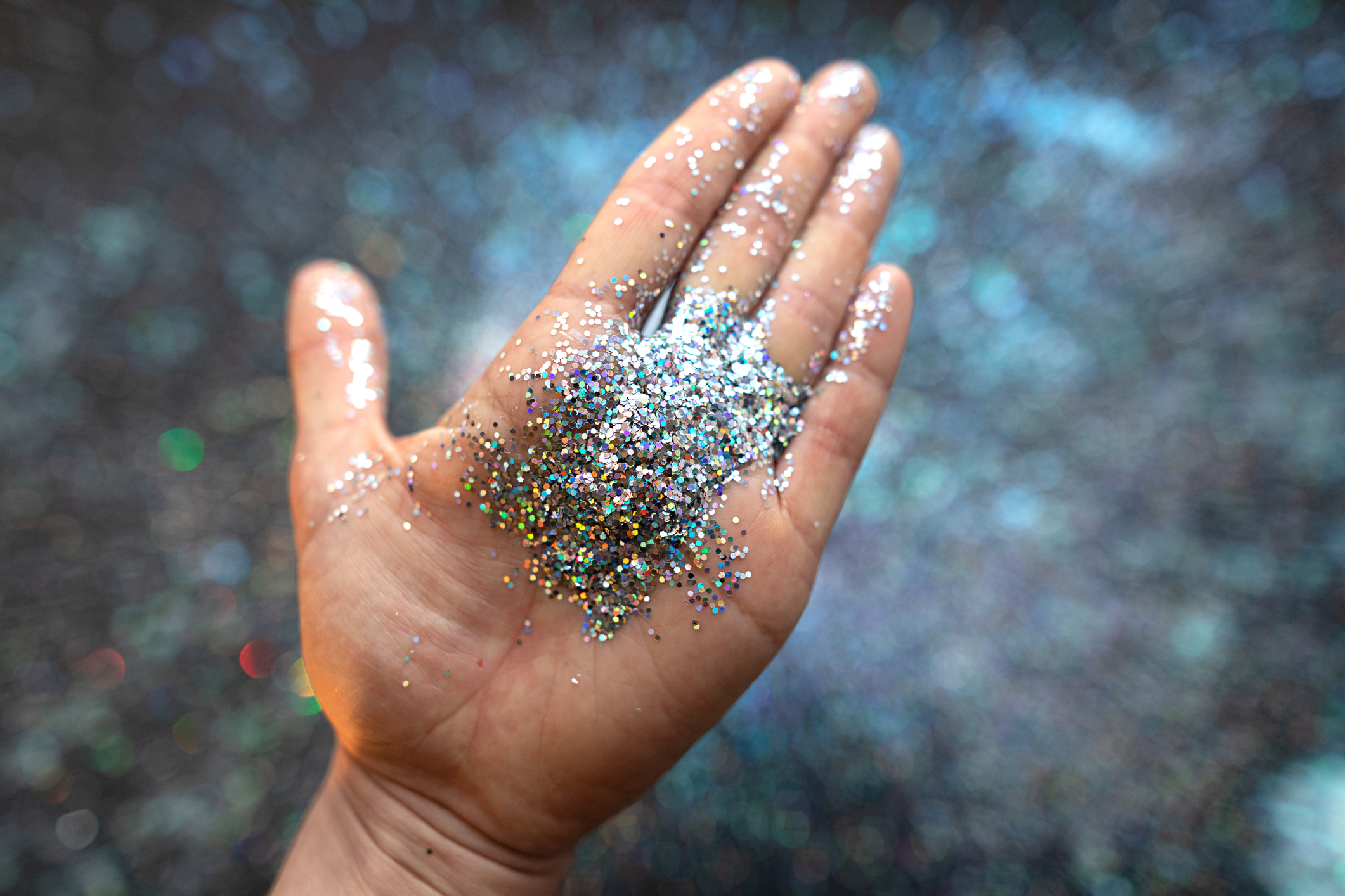 An open hand holding sparkling glitter with a blurred background
