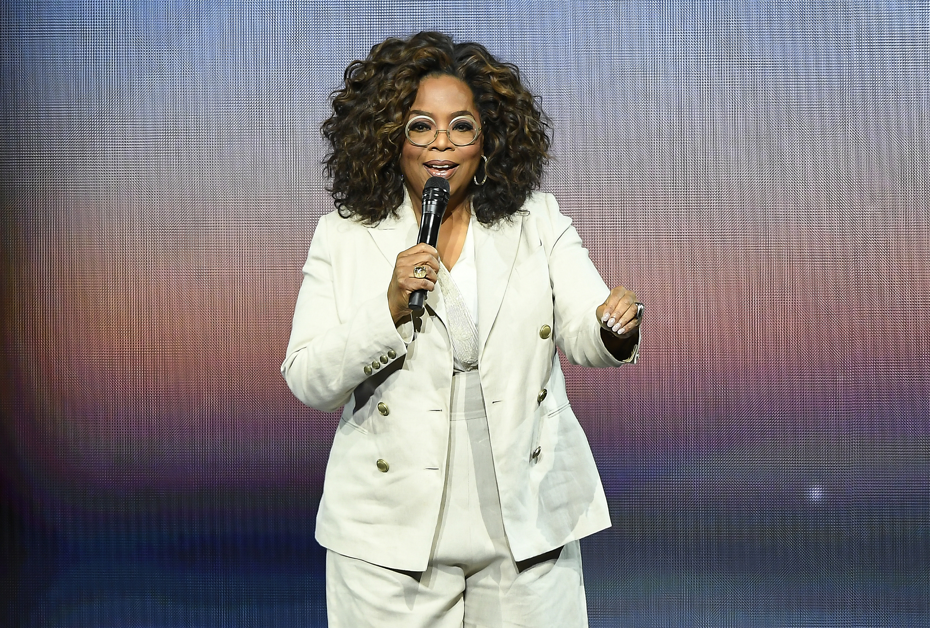 Oprah Winfrey speaking onstage, wearing a stylish suit