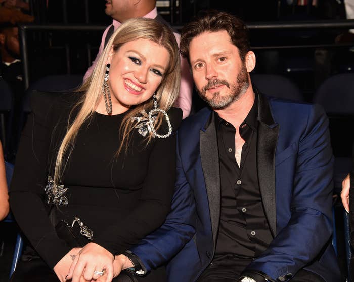 Kelly Clarkson and Brandon Blackstock sitting together at an event, Clarkson in a black dress with embellishments
