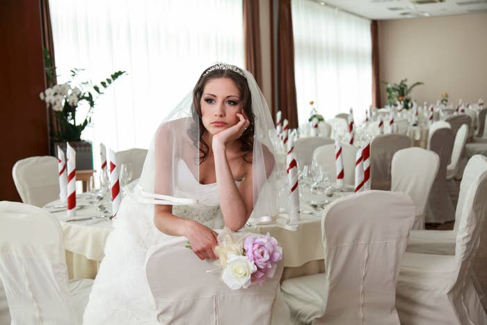 Bride in a wedding dress and tiara sitting at a table looking miserable