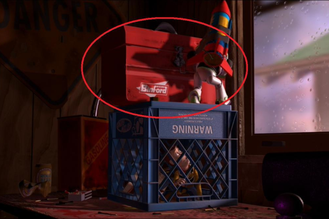 Blurry image of a toolbox with the name &#x27;Binford&#x27; on it, situated on a shelf above a crate labeled &#x27;Waltzinn.&#x27;