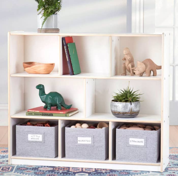 A shelving unit with toys, books, plants, and labeled storage bins