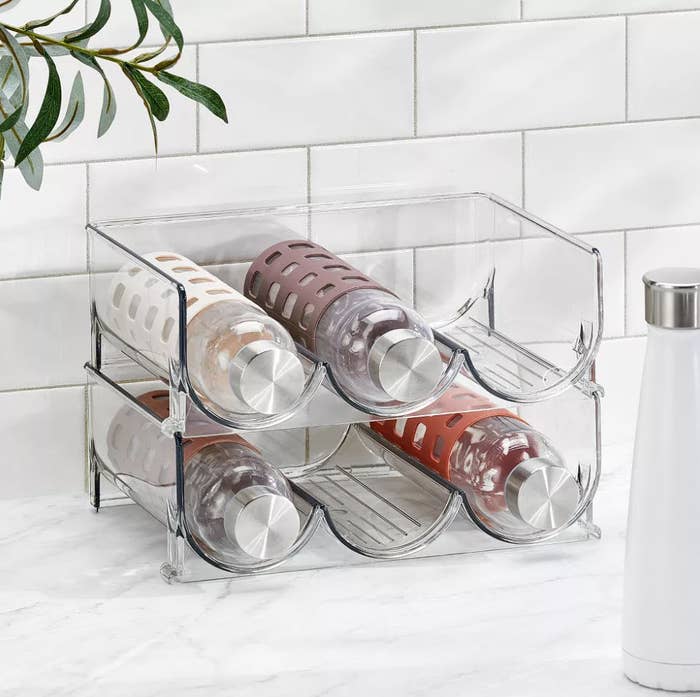 Clear acrylic water bottle storage rack with three bottles on a countertop