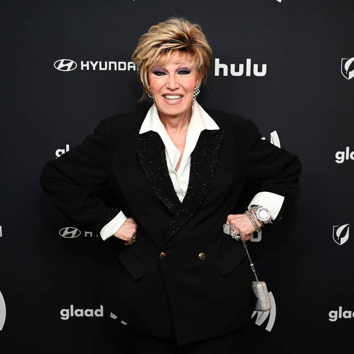 Closeup of her smiling, wearing a black suit, white shirt, and sequined cuffs at an event