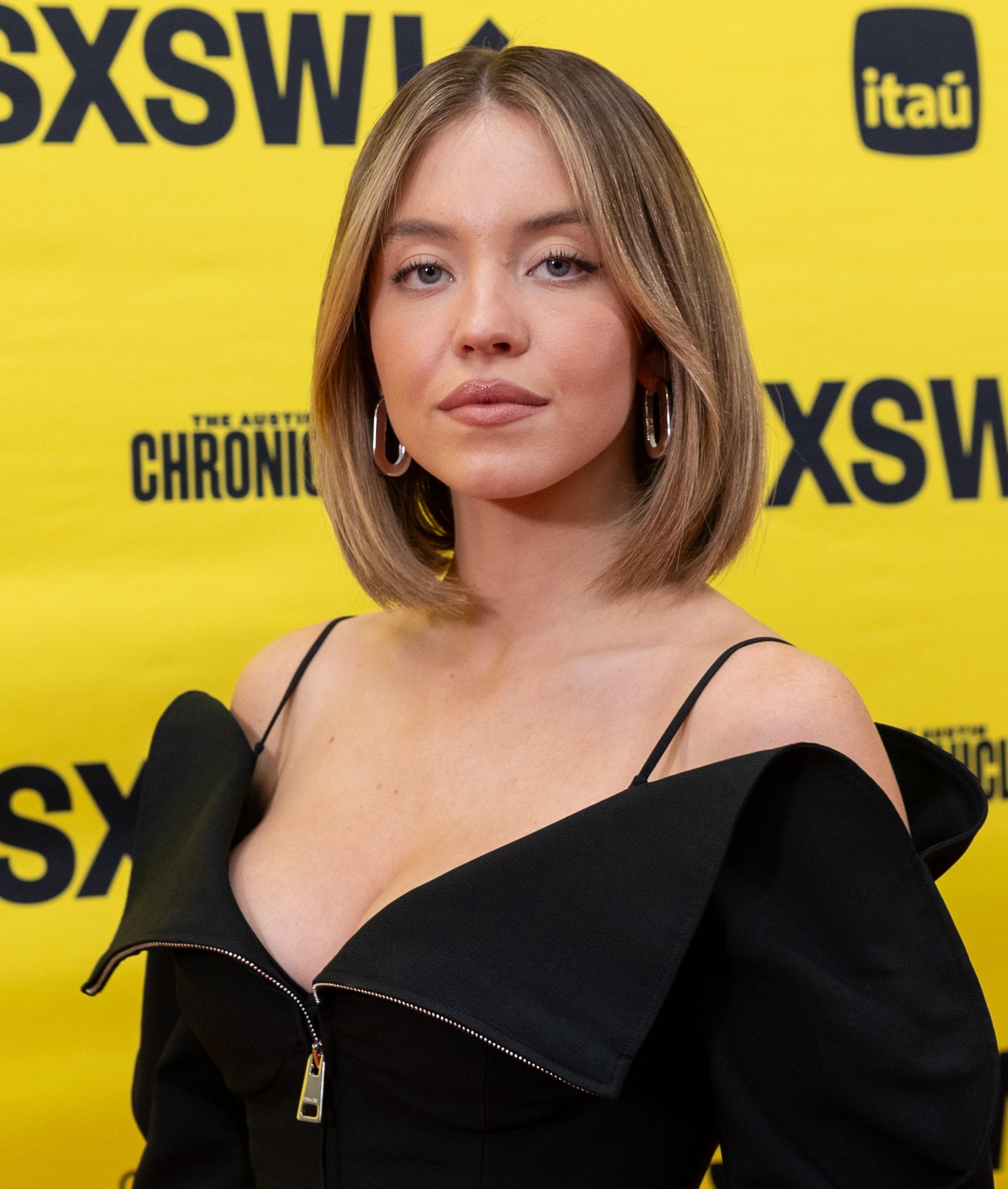 Sydney Sweeney posing at SXSW event in a black off-shoulder dress with a plunging neckline