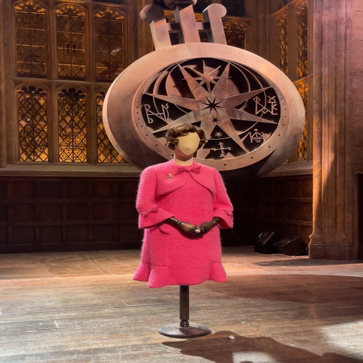 Mannequin displaying a pink tweed outfit with jacket and skirt, positioned in front of a large, intricate clock backdrop