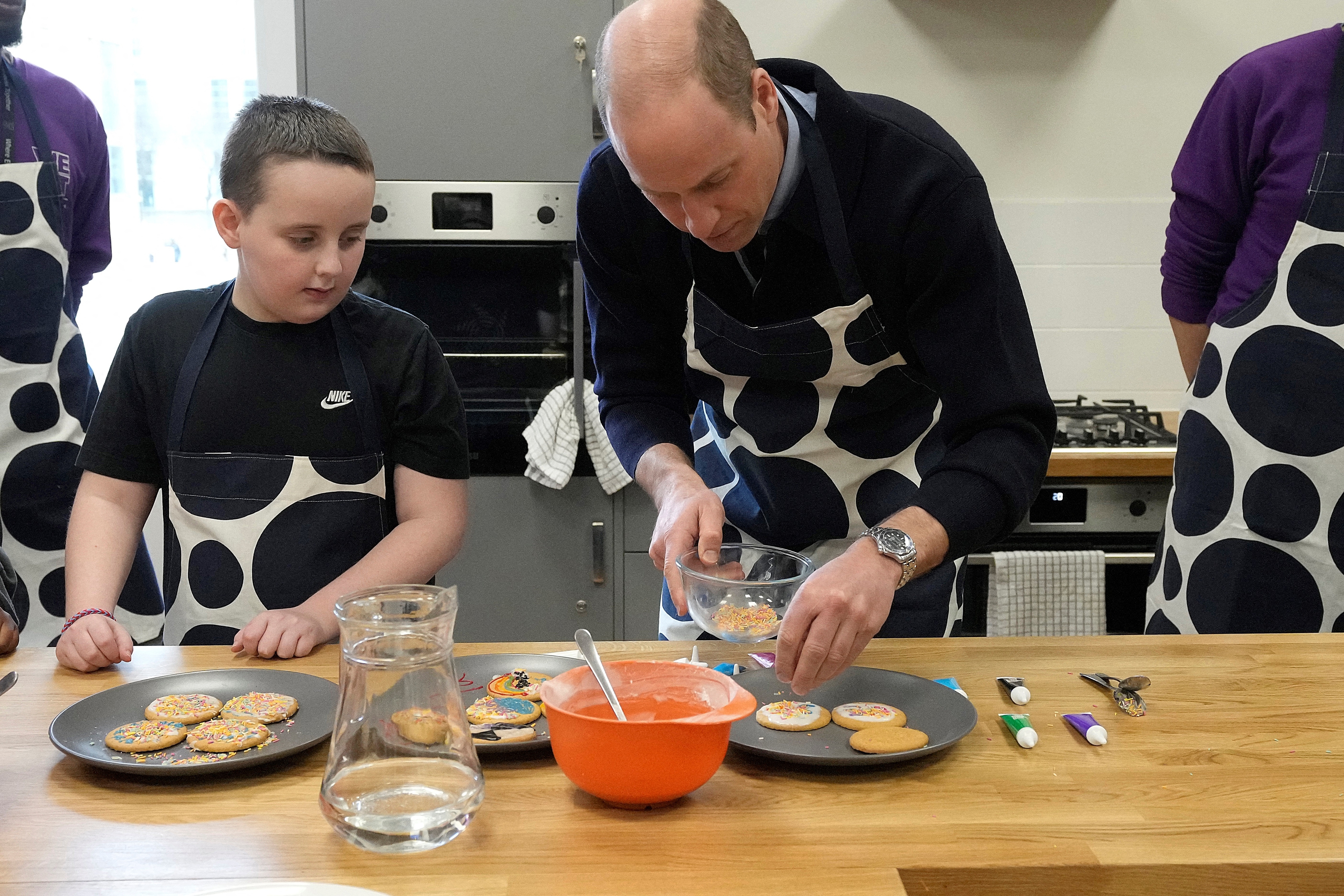 Prince William, apron-clad, cooks with a young boy in a kitchen setting