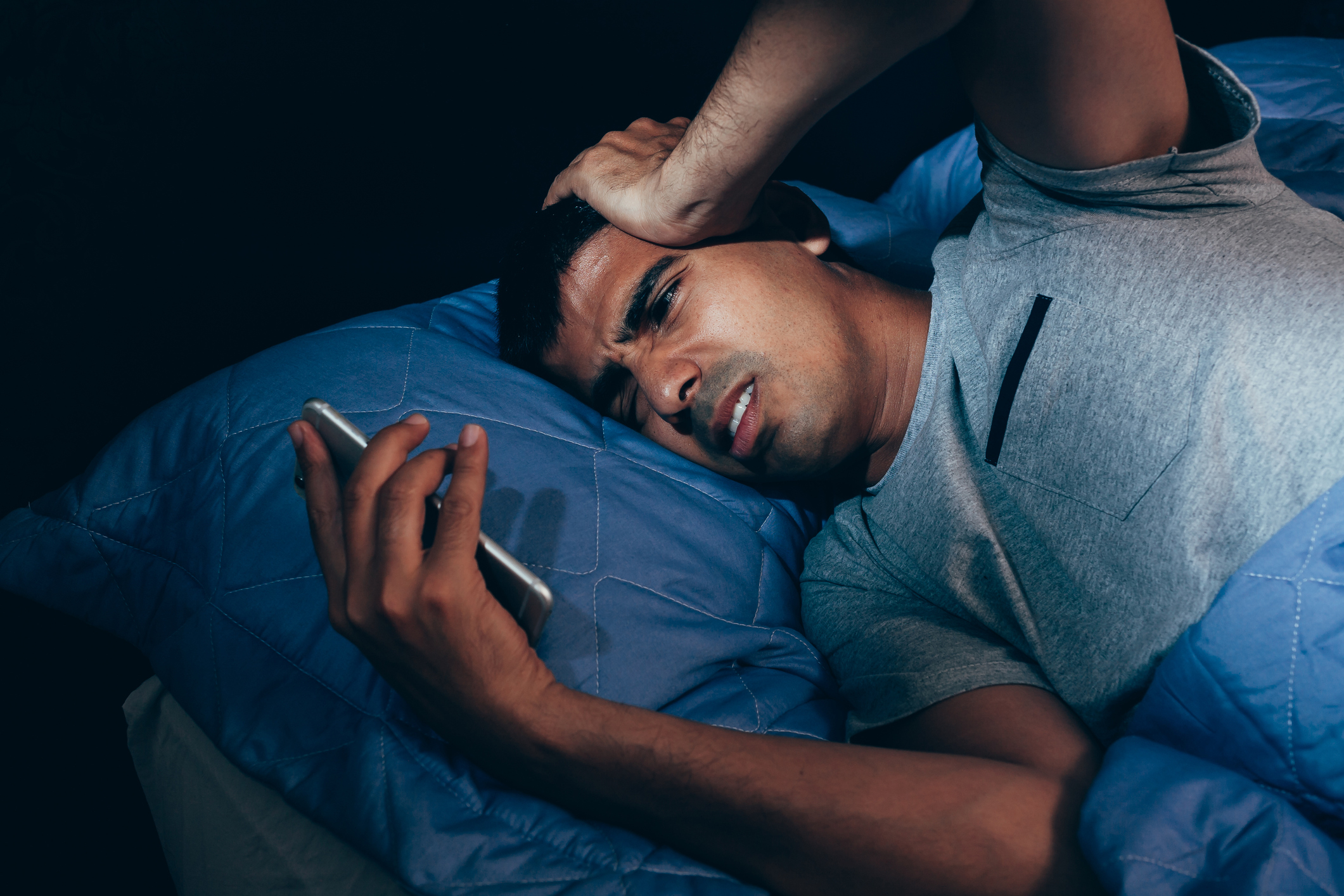 Man lying in bed holding a phone with a concerned expression