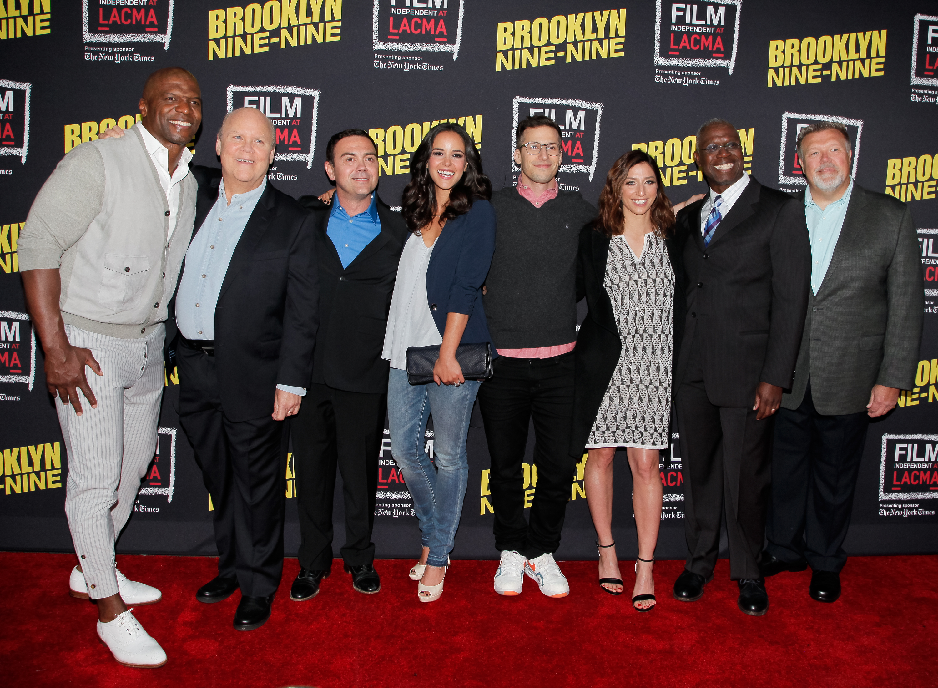 Cast of Brooklyn Nine-Nine standing together at an event in smart casual attire