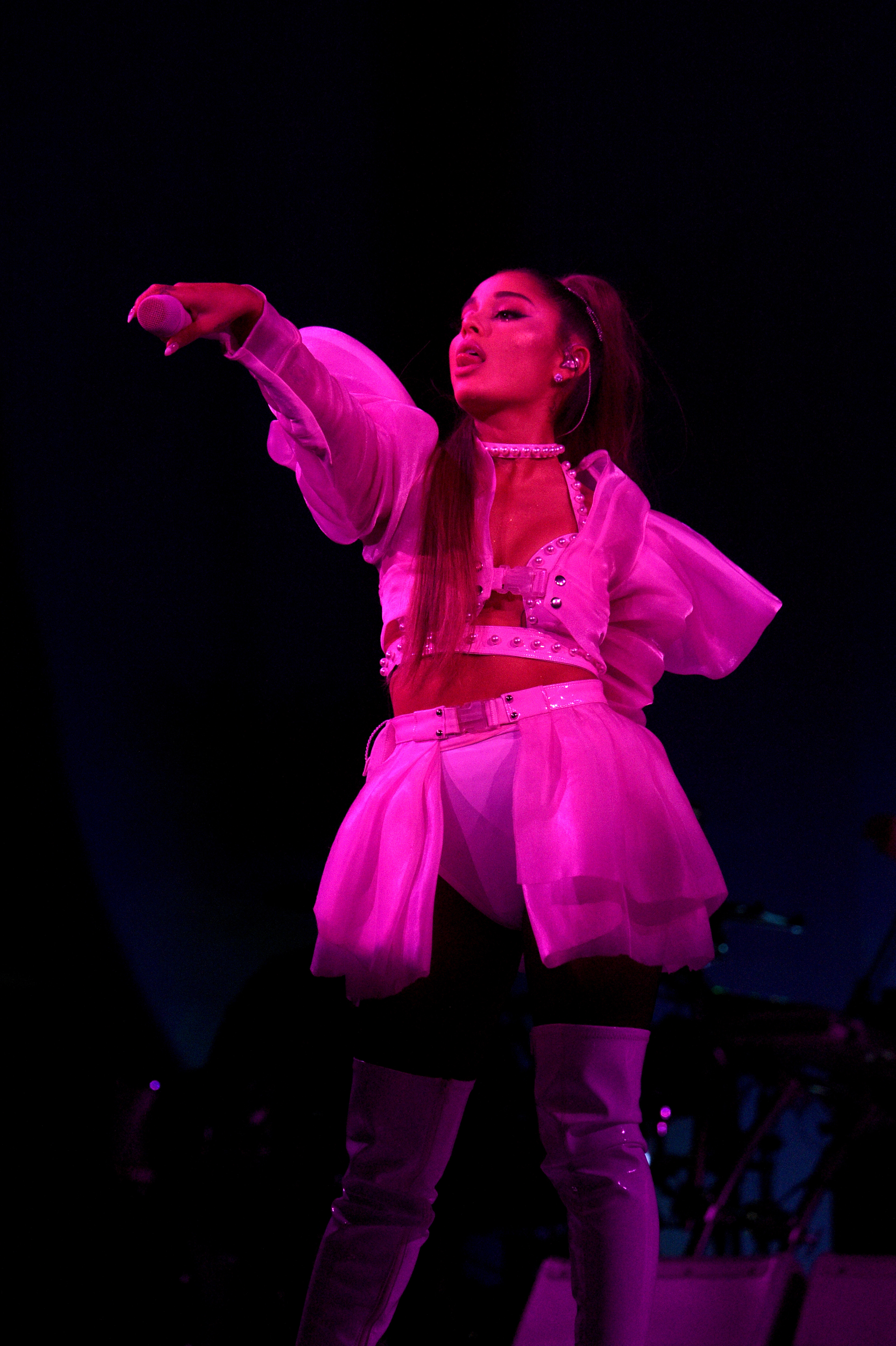 Ariana Grande performing on stage, wearing a stylish white outfit with knee-high boots