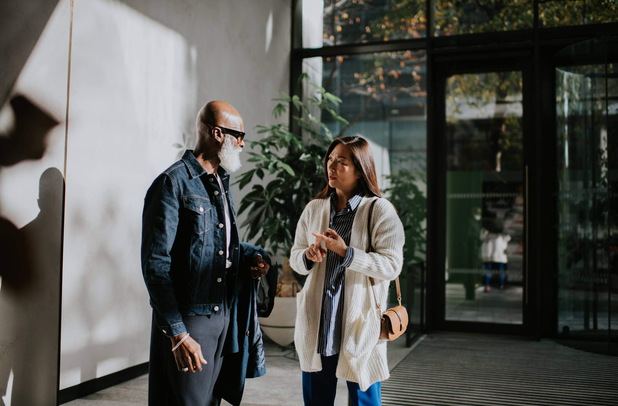 Two individuals appear to be engaged in a conversation with expressive gestures in a well-lit indoor setting