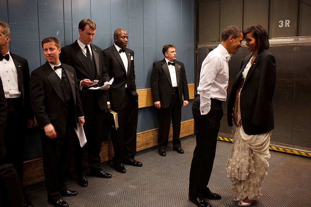 Barack and Michelle Obama touch foreheads, surrounded by aides, in a backstage elevator&#x27;s casual setting