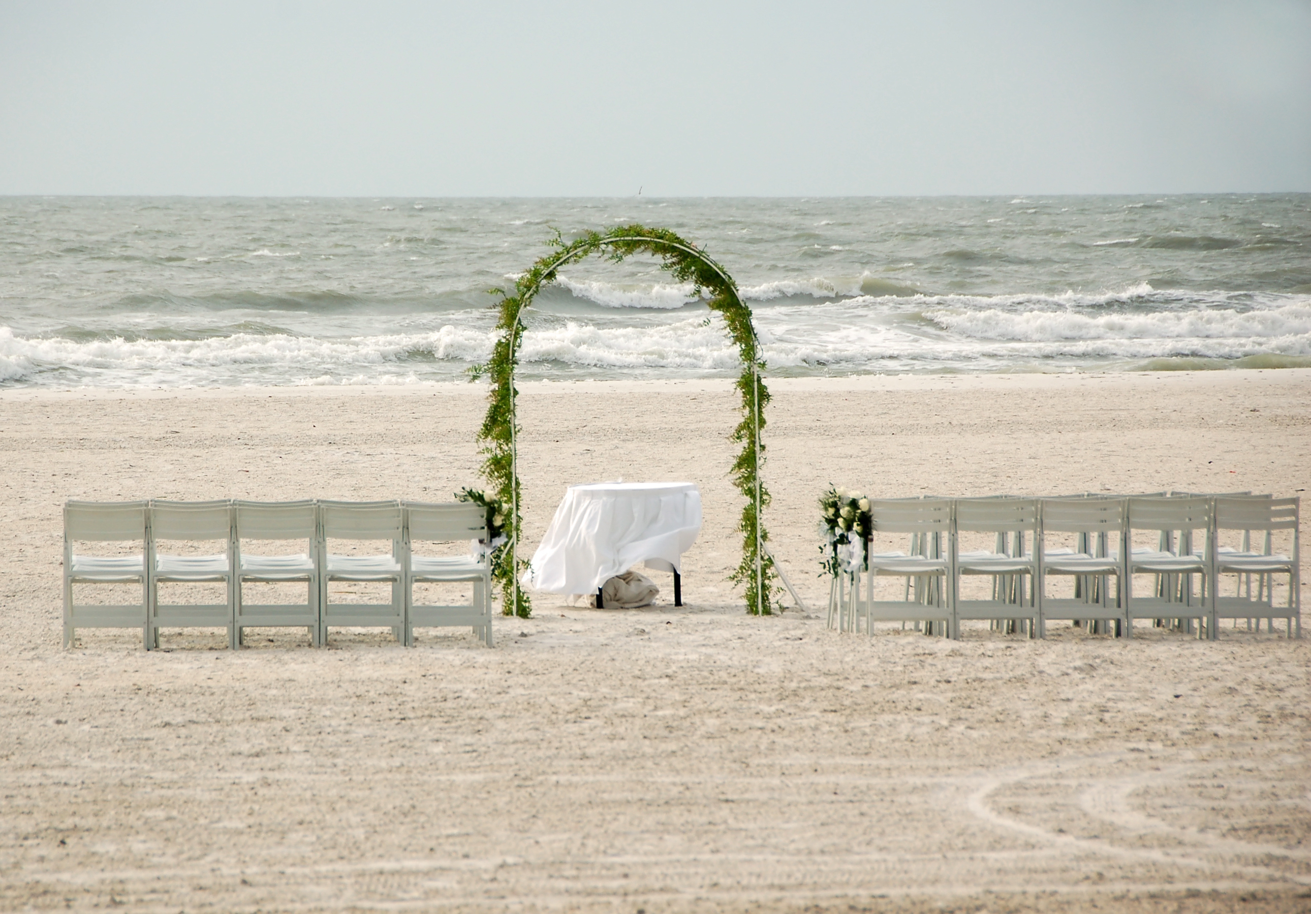 Beach wedding setup with an arch and rows of benches facing the ocean