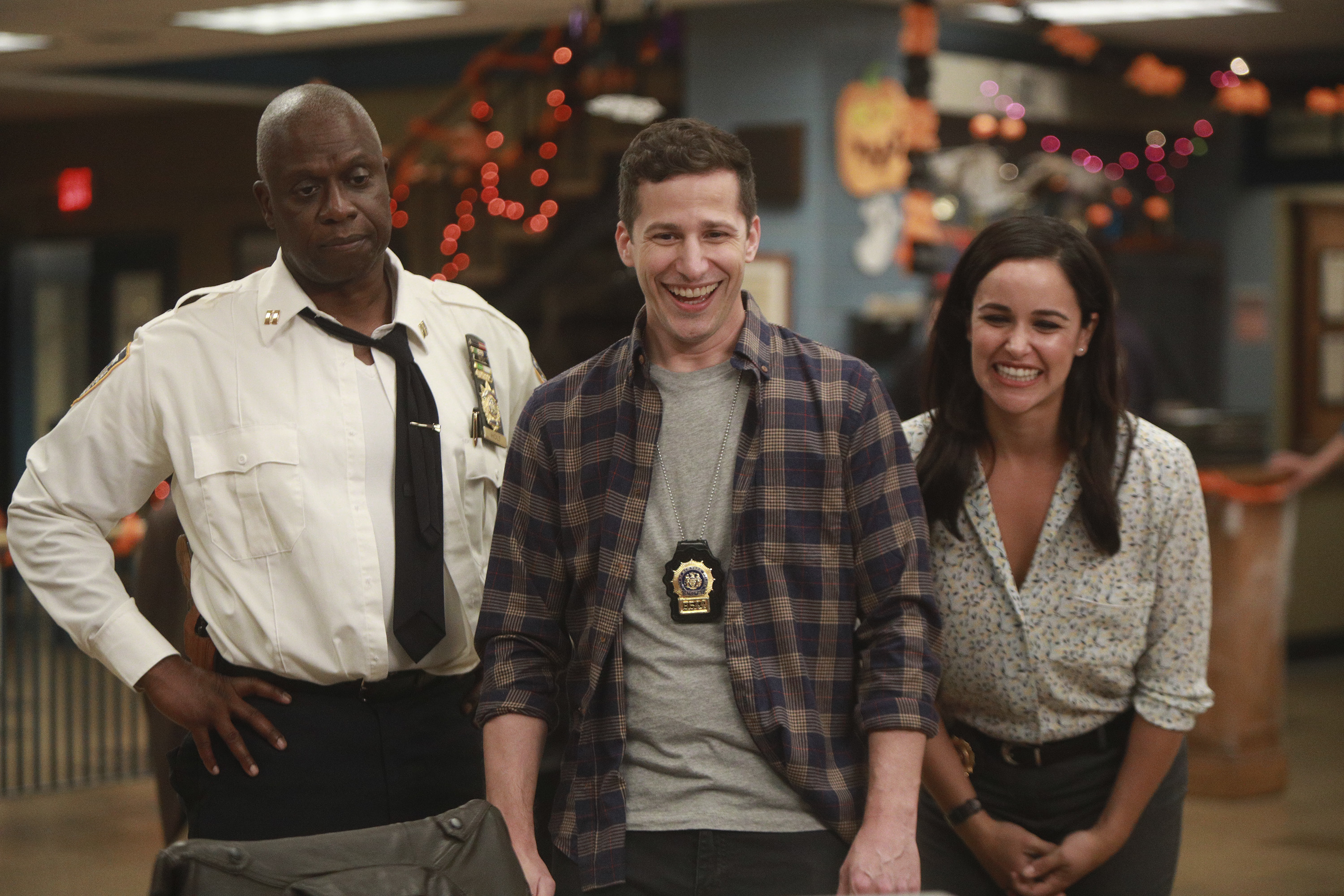 Three actors standing side by side in a police precinct setting from the TV show &quot;Brooklyn Nine-Nine.&quot;