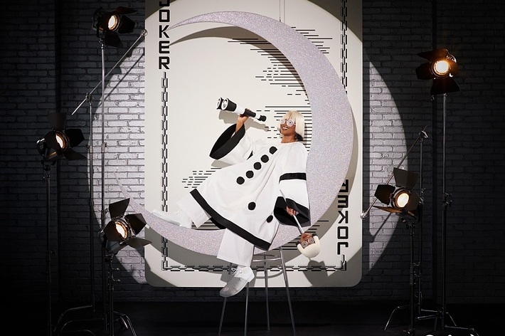Album cover with artist in a futuristic white outfit posing inside a large letter 'C' surrounded by studio lights