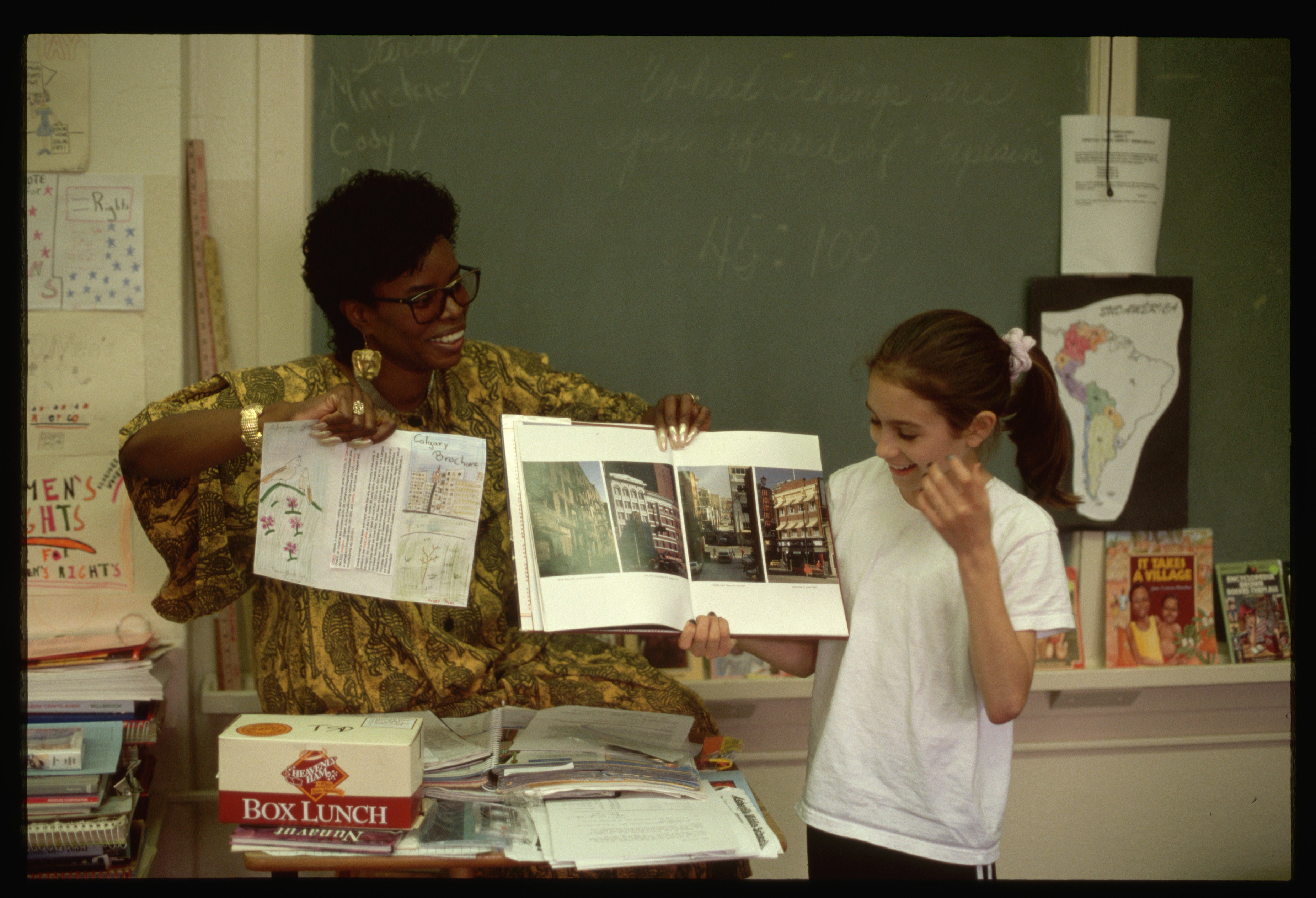 Teacher showing a student a book in a classroom with educational materials around