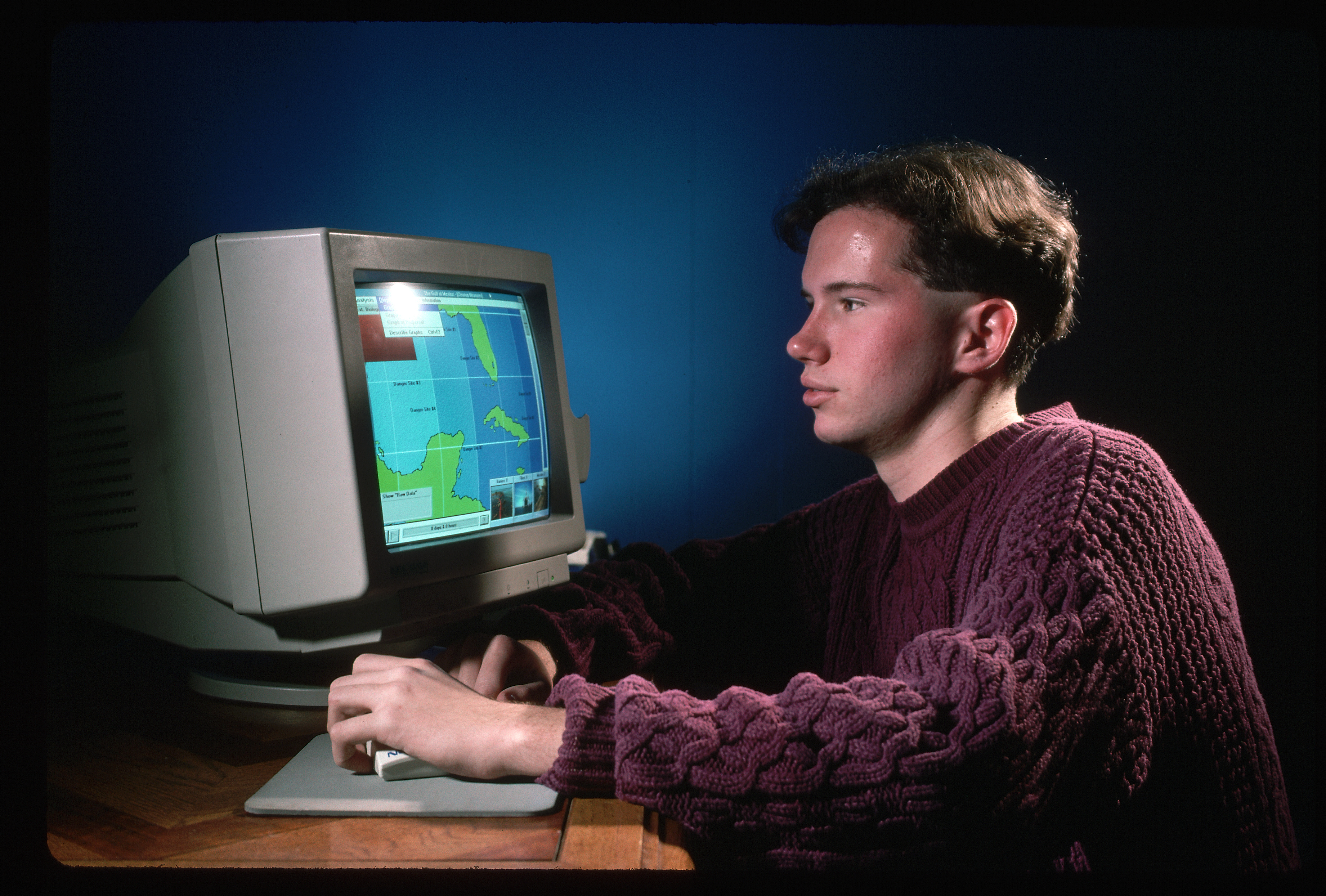 Person using an old computer with a map on the screen, wearing a sweater