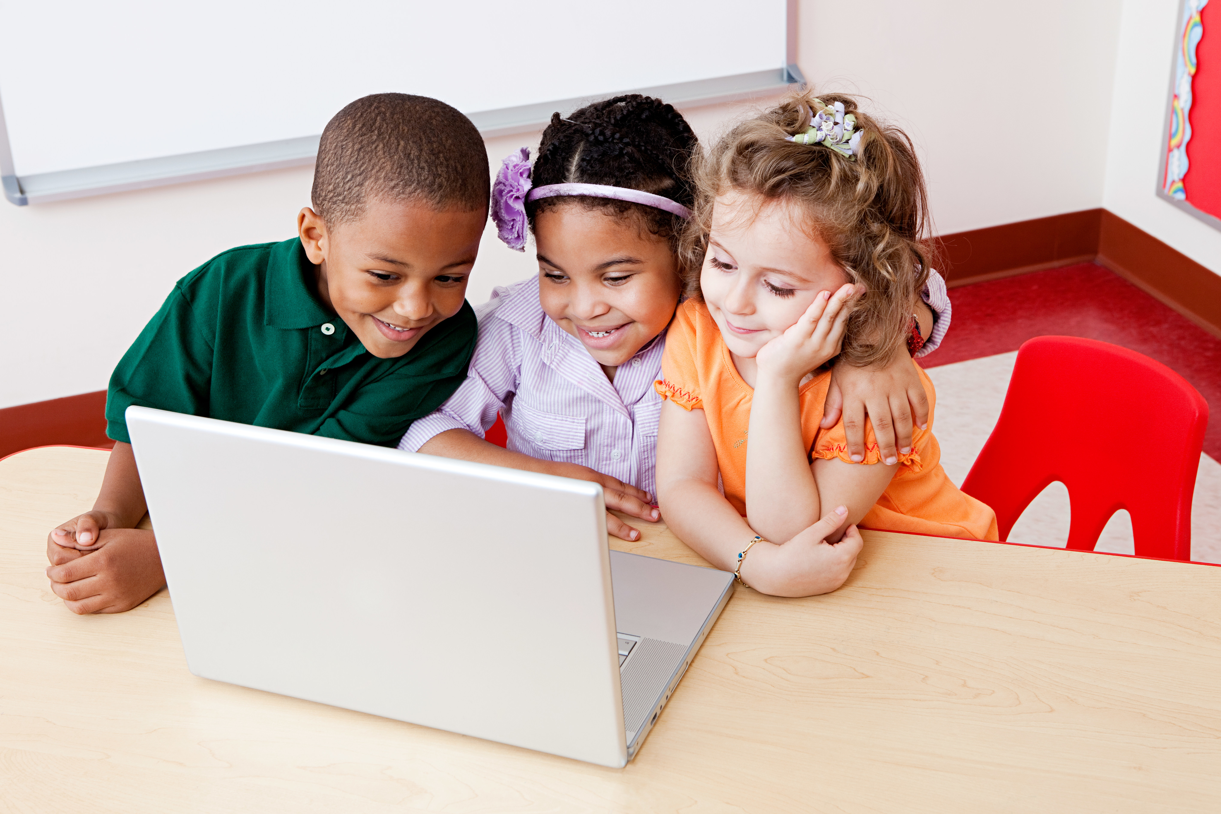 Three children are gathered around a laptop, appearing engaged and happy