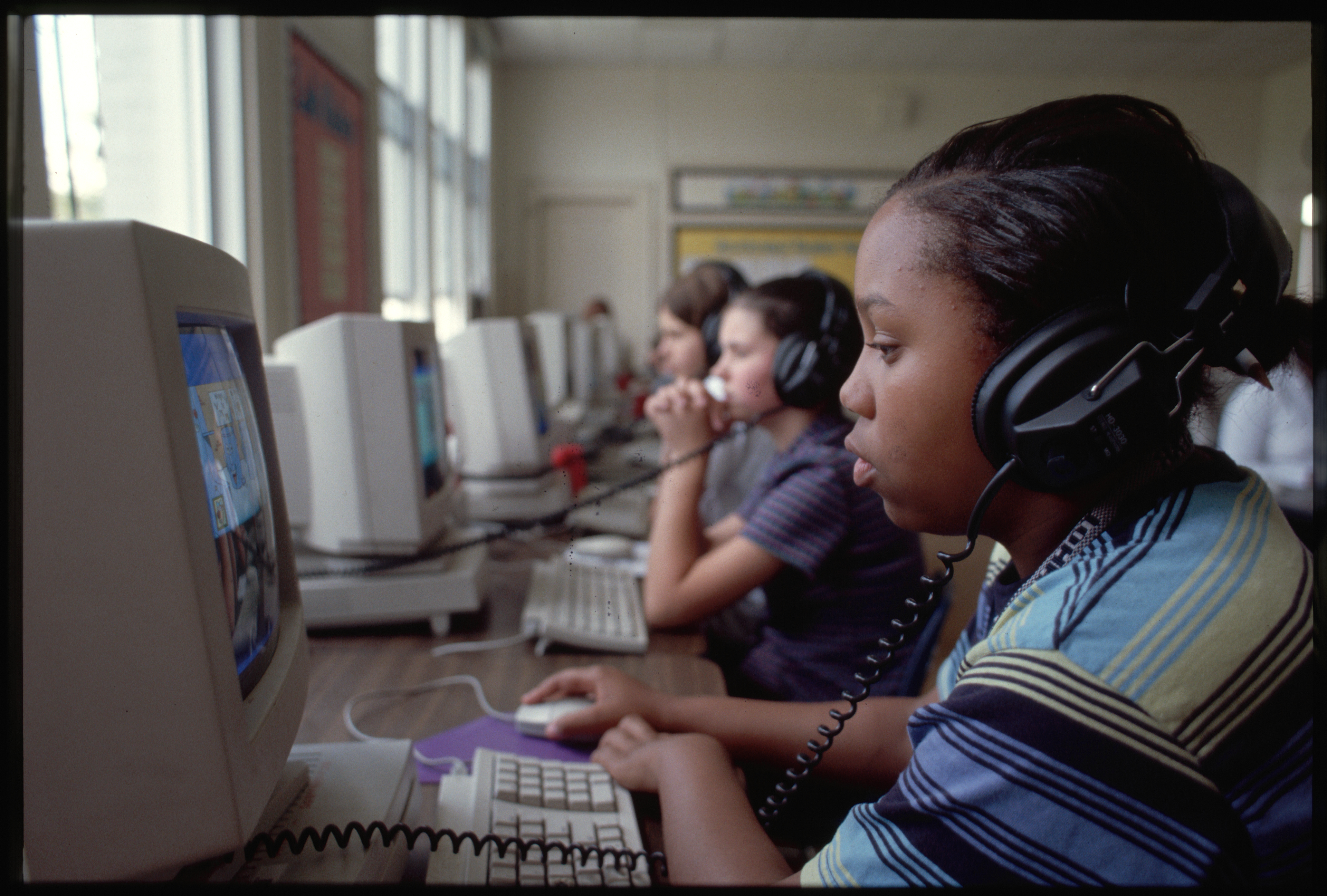 Students at computers with headphones, focusing on screens, educational setting