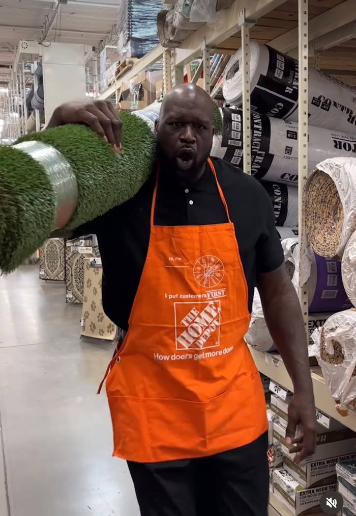 Shaquille O&#x27;Neal in a Home Depot apron assisting a customer with carpet rolls