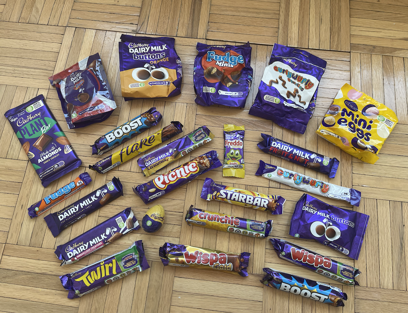 Assorted Cadbury chocolates and snacks laid out on a wooden floor