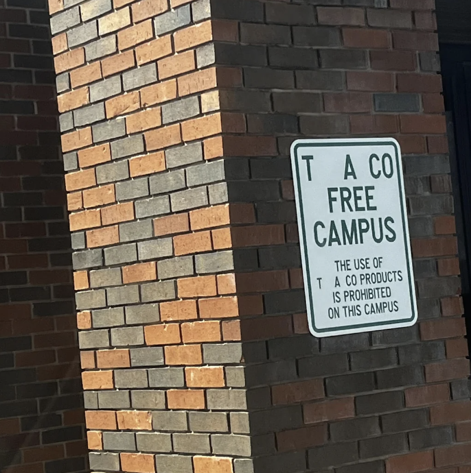 Sign on brick wall stating campus is tobacco-free, banning use of such products, but someone made it spell &quot;TACO&quot;