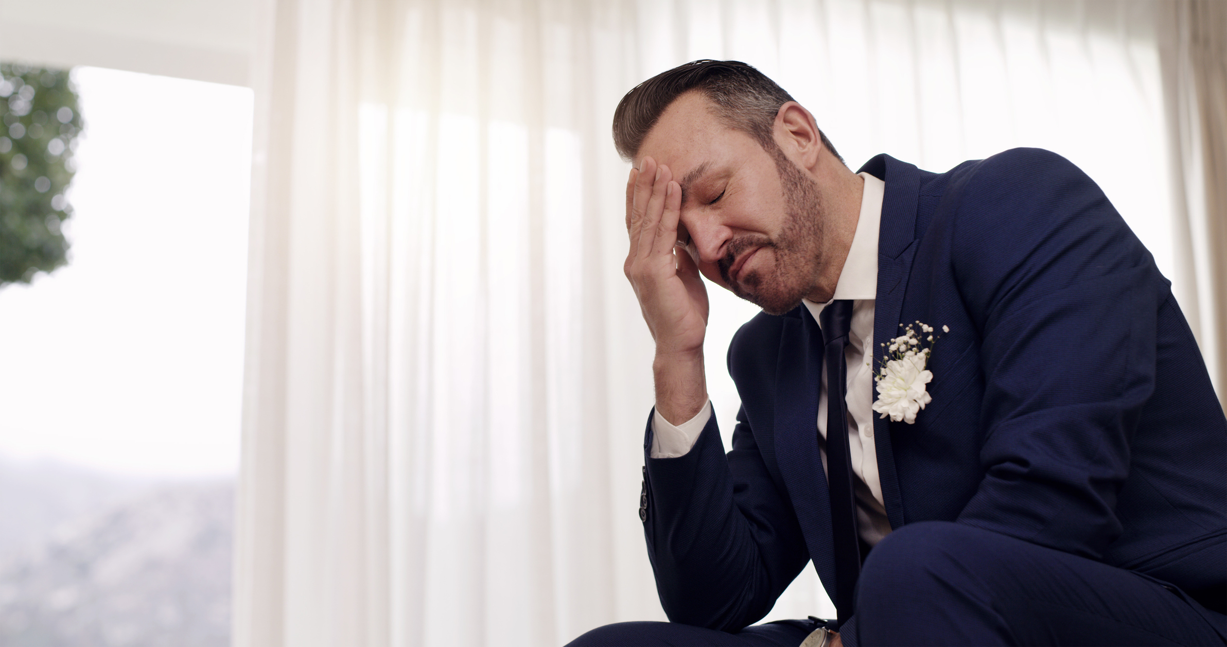 Groom in a suit with boutonniere sitting emotionally with his hand on his forehead